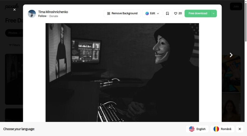 Hacker cu masca lucrand pe computer, simbolizand amenintarile de pe dark web